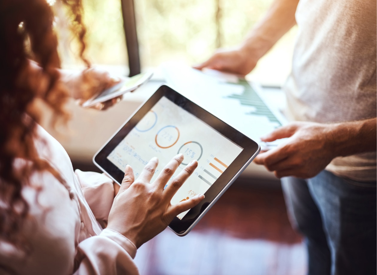 Image looking over a woman's shoulder as she holds a tablet and reviews analytics.