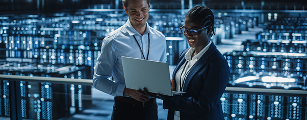 Image shows a man and a woman smiling together as they look at a laptop with server banks in the background. Related to: designing for future demand, architectural foundation, cyber architecture foundation, digital architecture services, digital architecture as a service,