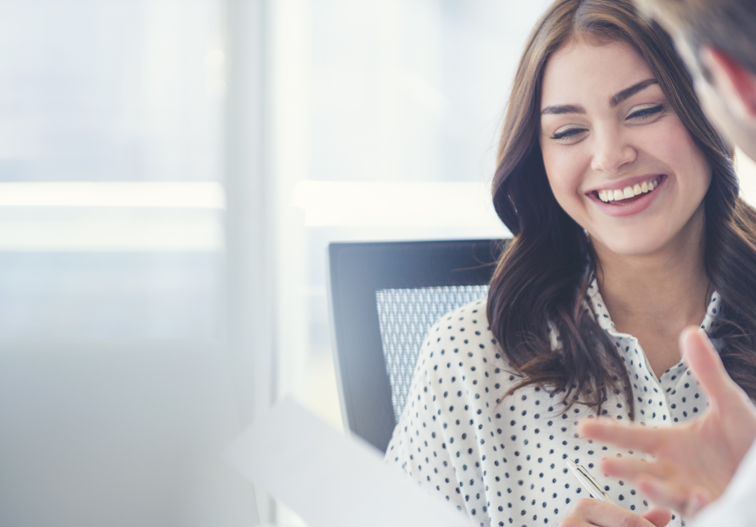 Image of a woman smiling as she looks at a piece of paper and listens to a man talking to her.