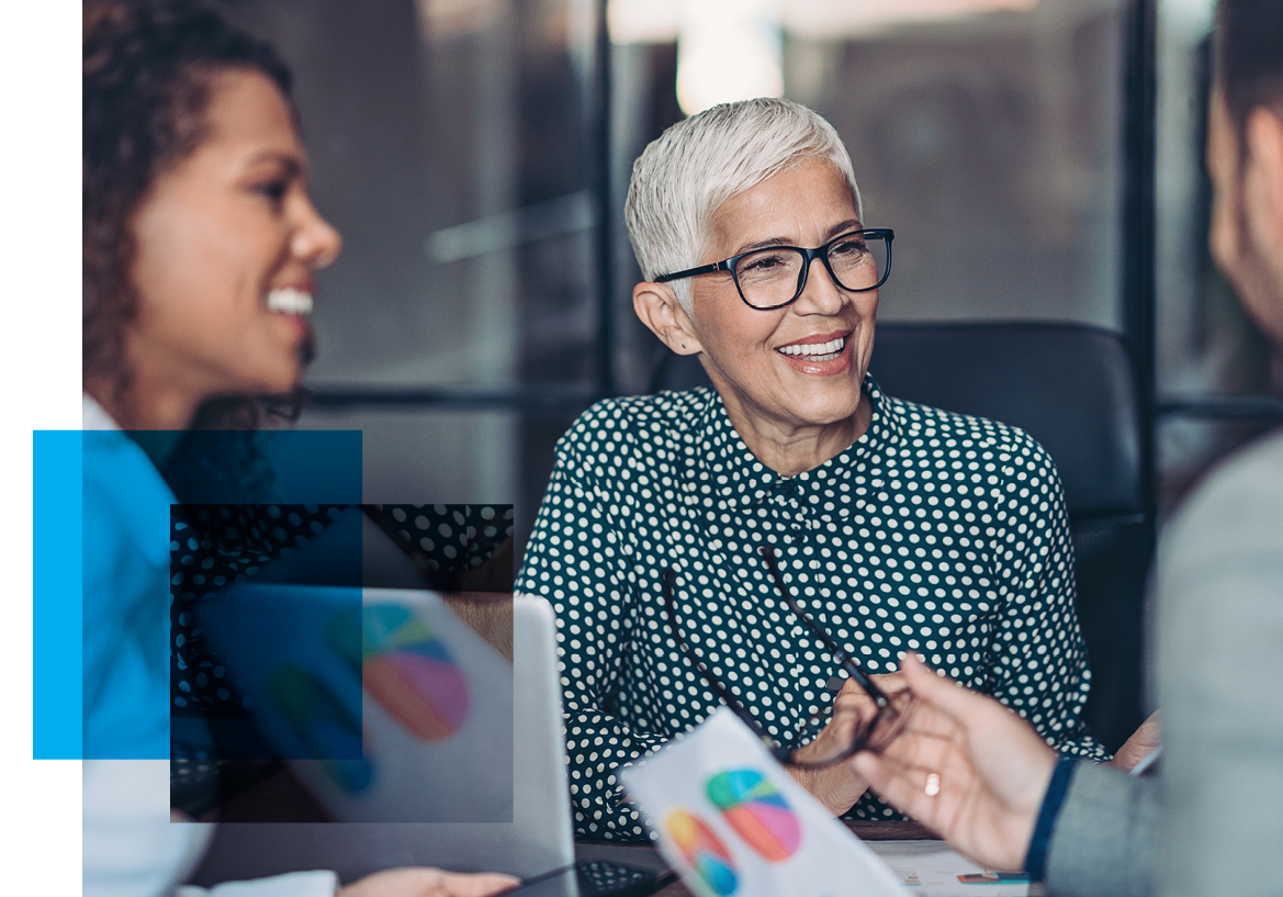 Image of an older woman with glasses smiling at a man who's talking while another woman also listens in. Related to: sr proposal writer job, senior proposal writer job, managing editor job, Staff Writer job, researcher job, capture manager job, Management Analyst job,