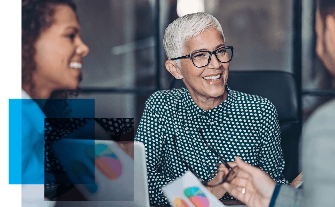Image of an older woman with glasses smiling at a man who's talking while another woman also listens in. Related to: sr proposal writer job, senior proposal writer job, managing editor job, Staff Writer job, researcher job, capture manager job, Management Analyst job,