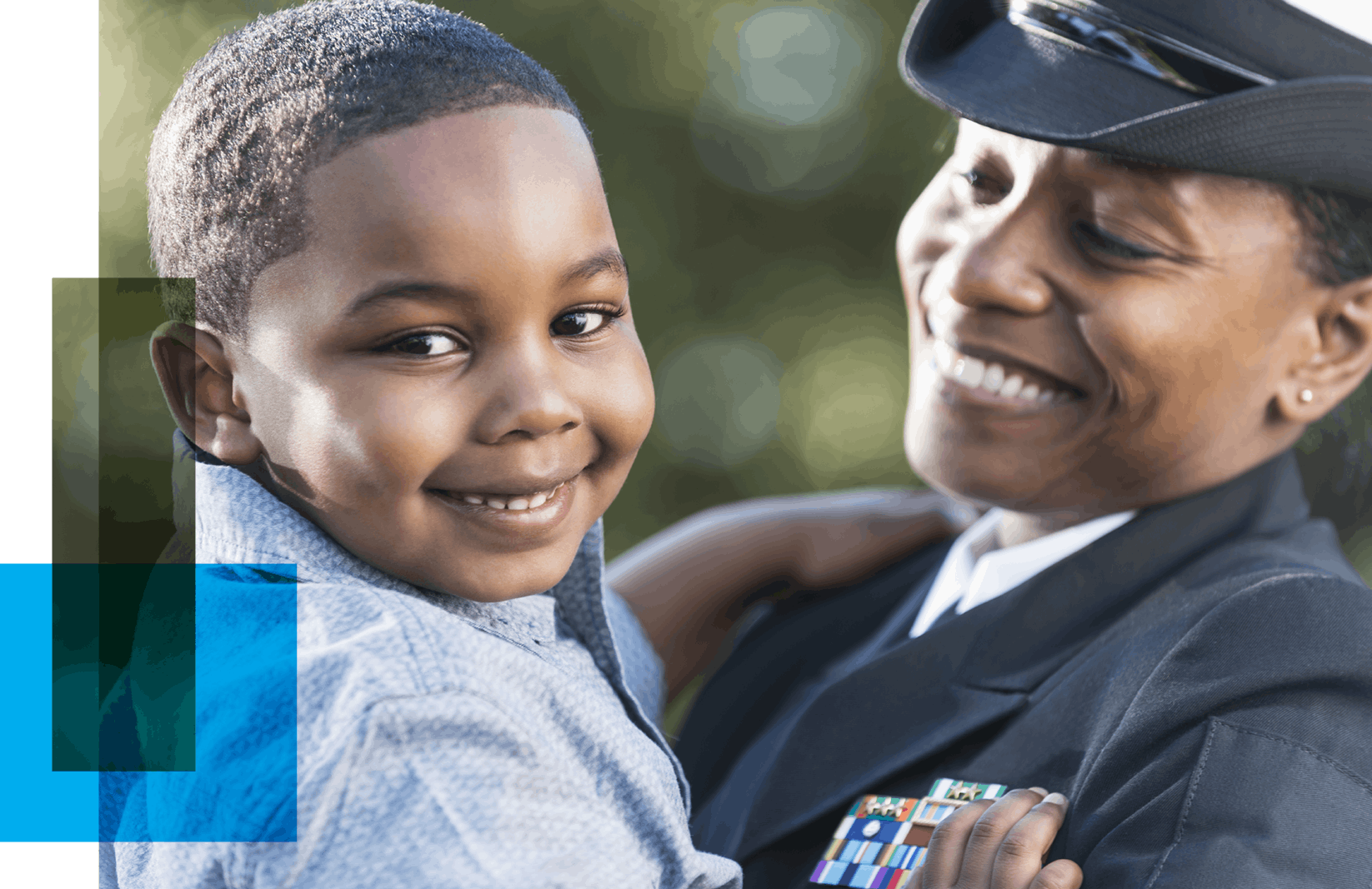 Image shows a black woman in naval uniform holding her child and smiling. The boy looks at the camera, also smiling.