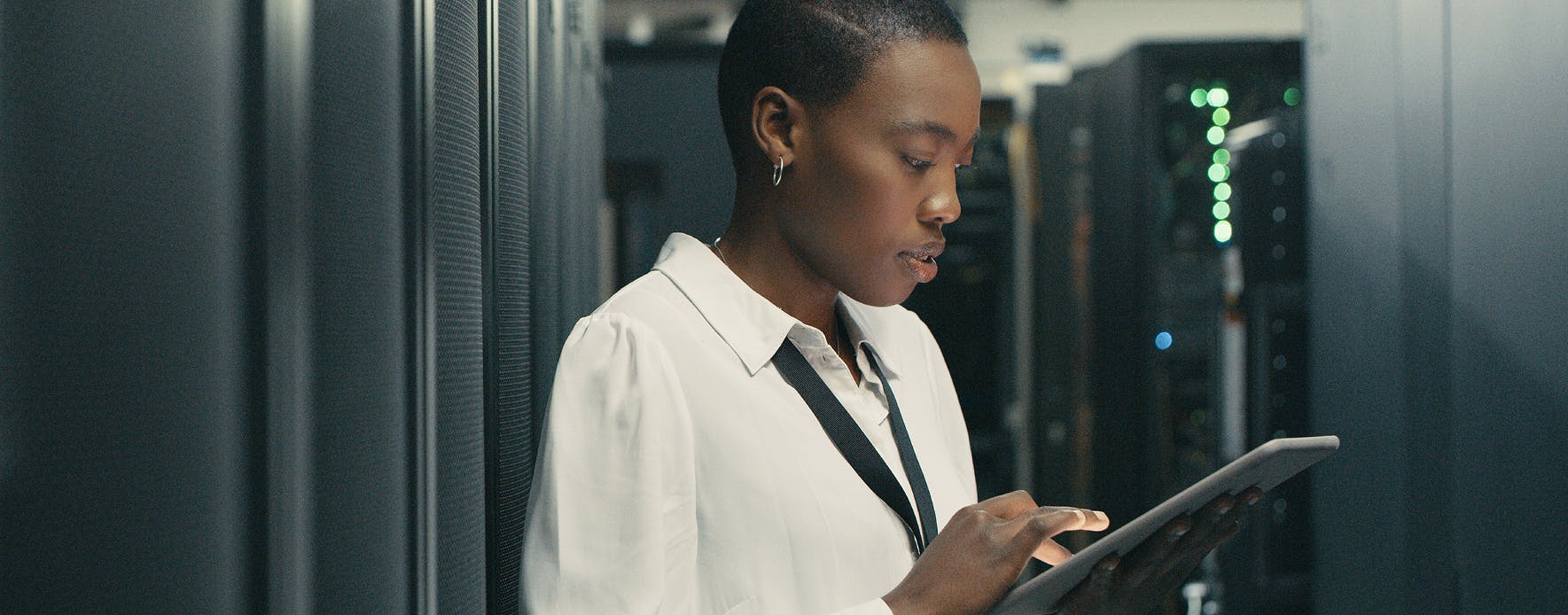 Image shows a black woman checking a tablet with servers in the background. Related to cyber engineering, cyber warfare engineer, cyber operations officer