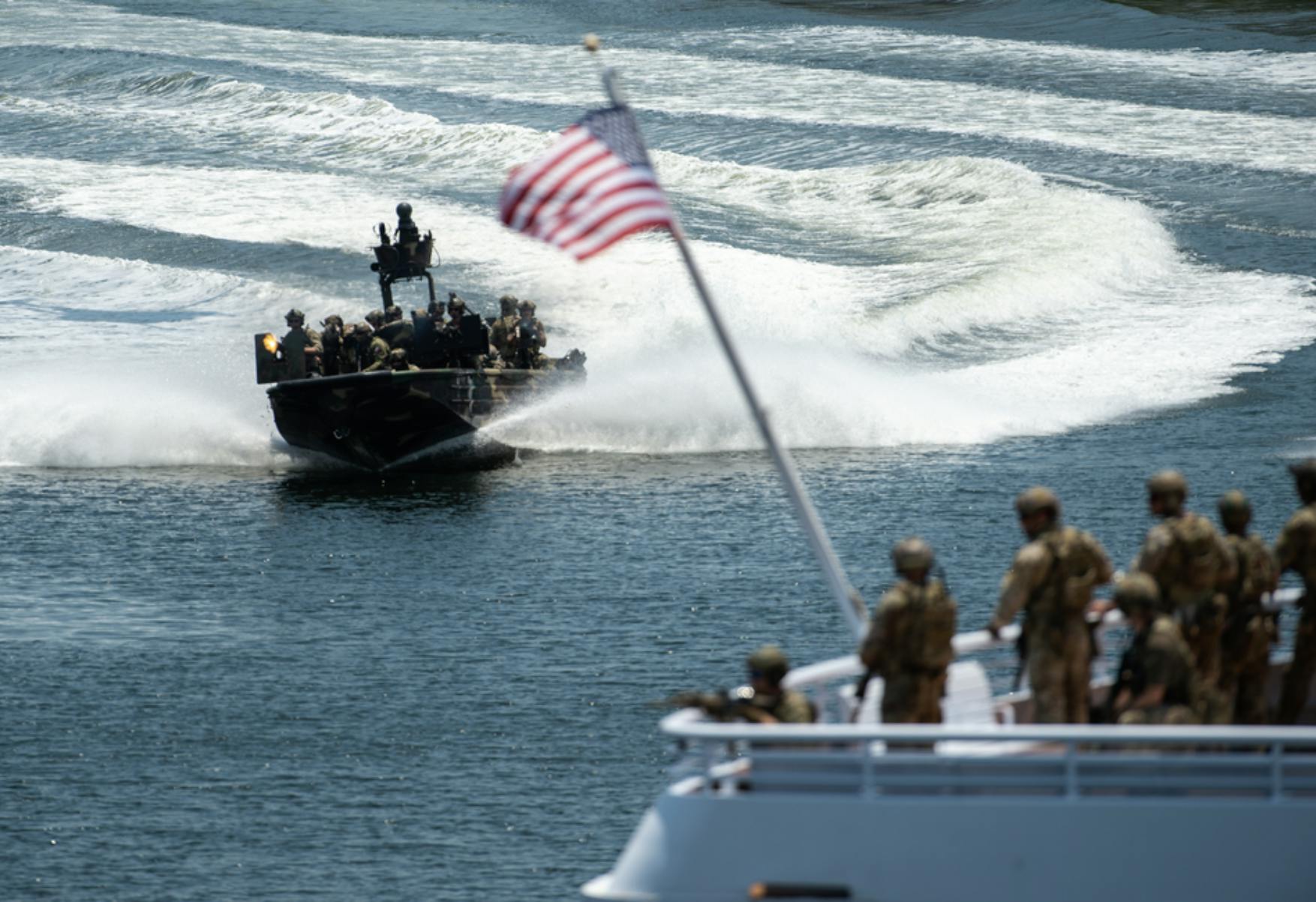 Image of a speed boat full of soldiers heading towards a larger cutter also with soldiers and the American flag hanging off the bow. Related to: navy digital modernization, ai digital transformation