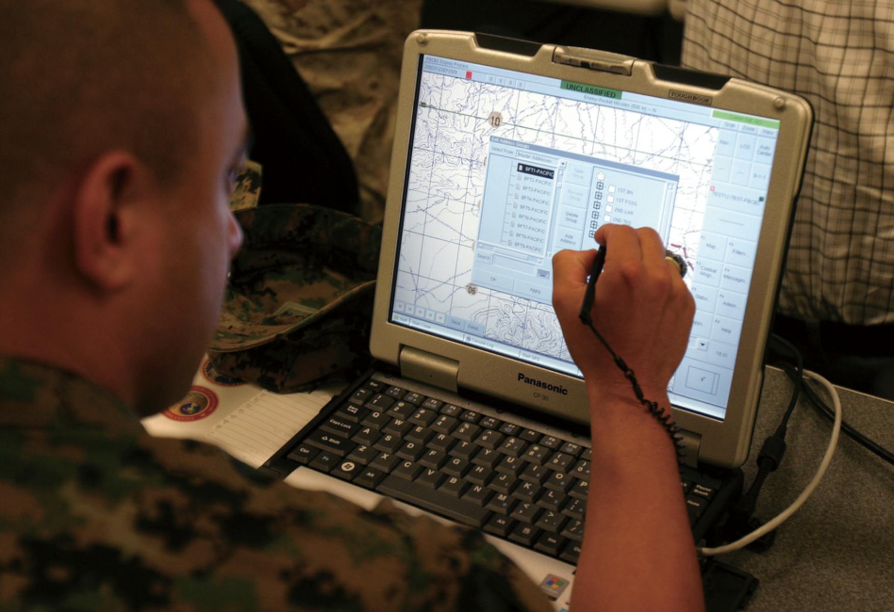 Image overlooking shoulder of a soldier in fatigues looking at a laptop screen and filling in information. Related to: data architecture, modernized systems, data modernization strategy, data ecosystem, federal data ecosystem, and data modernization goals.