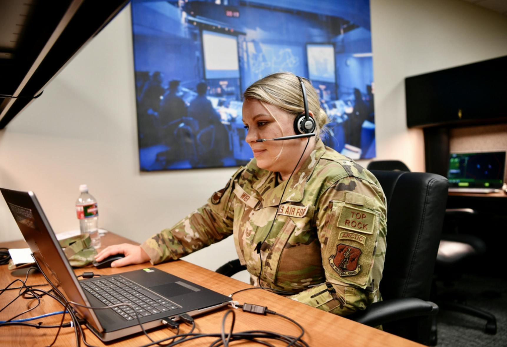 Woman in fatigues sits at desk with headphones on and looking at laptop in front of her. Related to: chief digital officer, dod CDO, dod mission, ai talent, artificial intelligence experts.