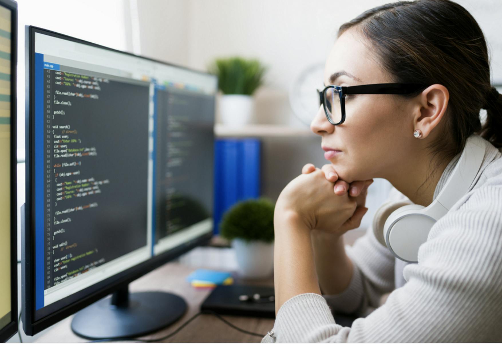 Image of a woman wearing glasses leaning towards a computer screen with code on it. Related to: devsecops user experience, user experience at gsa, software development frameworks improving customer experience.