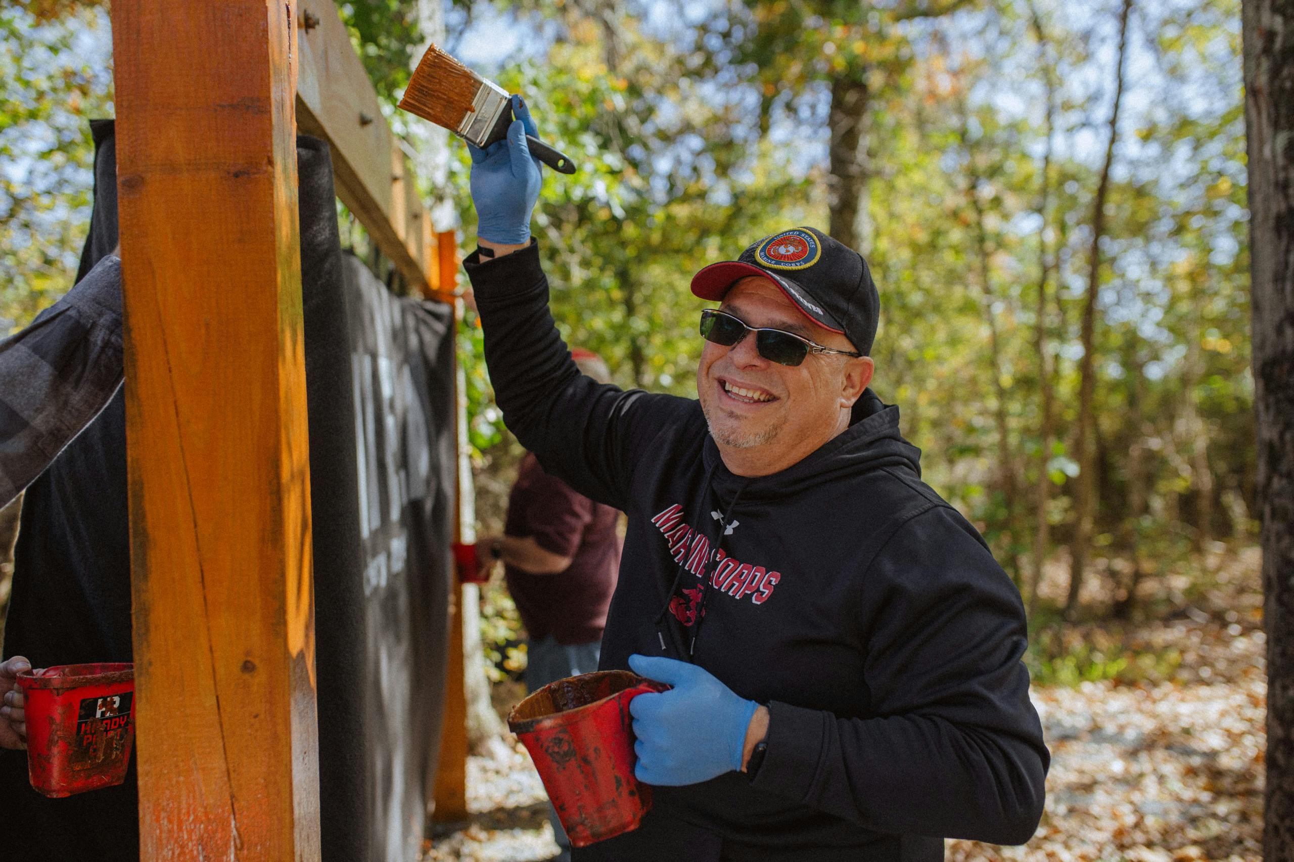 Image of a smiling man holding a paint can while he paints a sign.