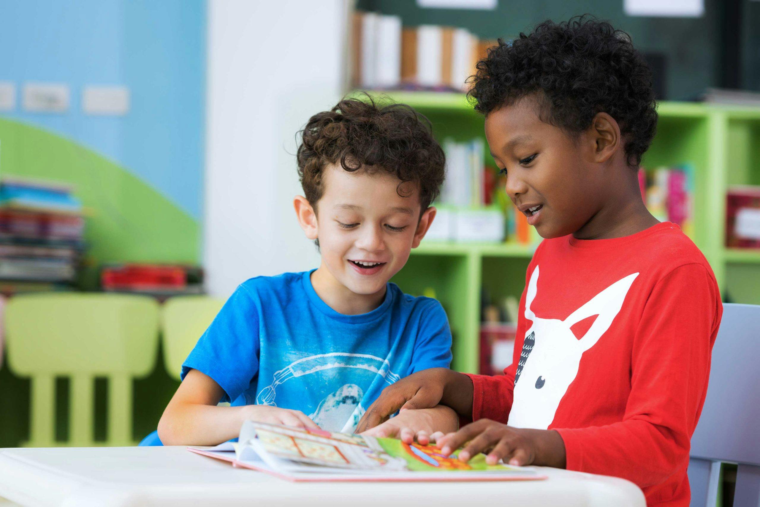 Image of two young children, one white and one black, looking down at a workbook in a classroom.