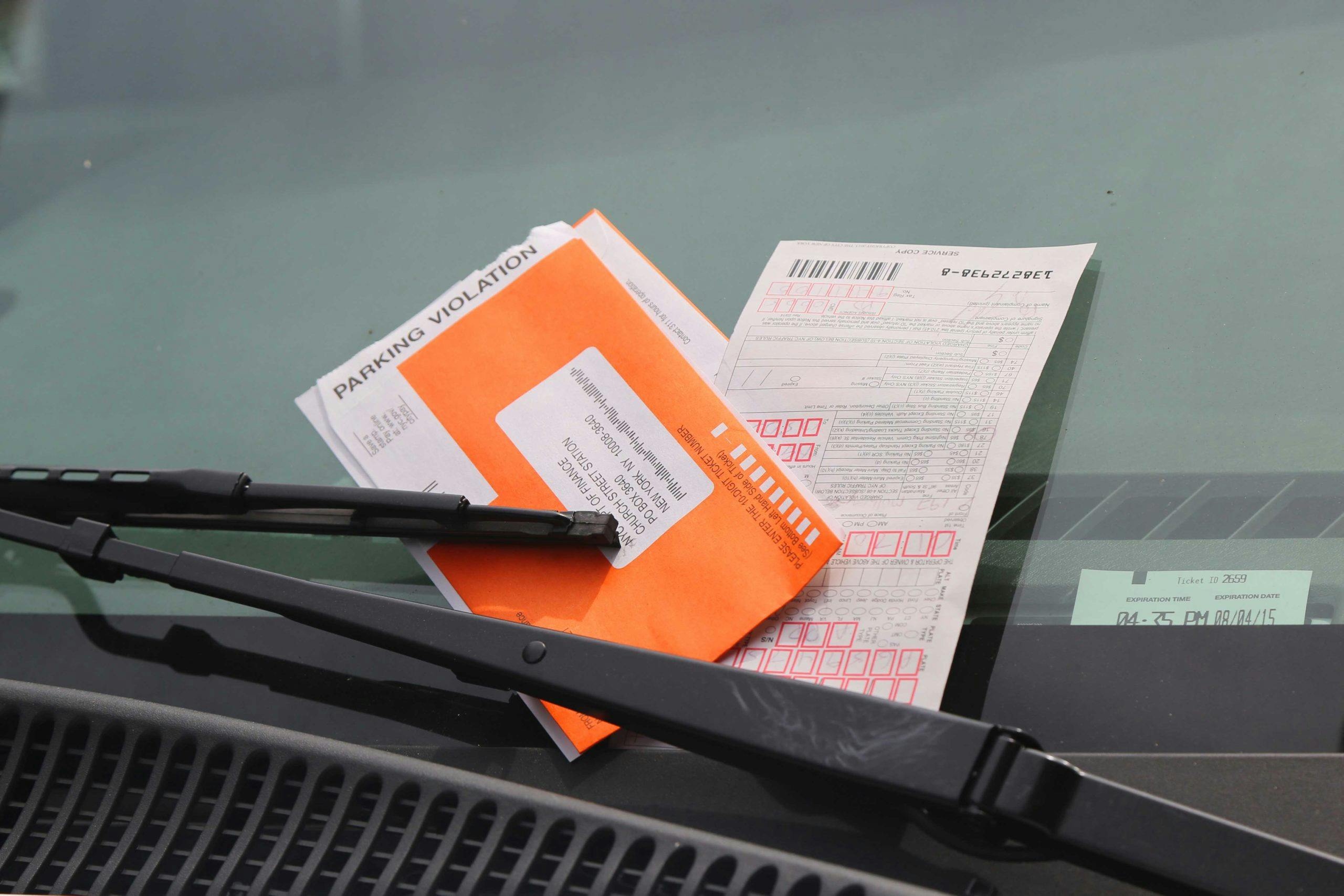 A cropped image of a windshield and windshield wipers with parking tickets tucked under the wipers. Accompanies the header for Voyager Parking Violations.