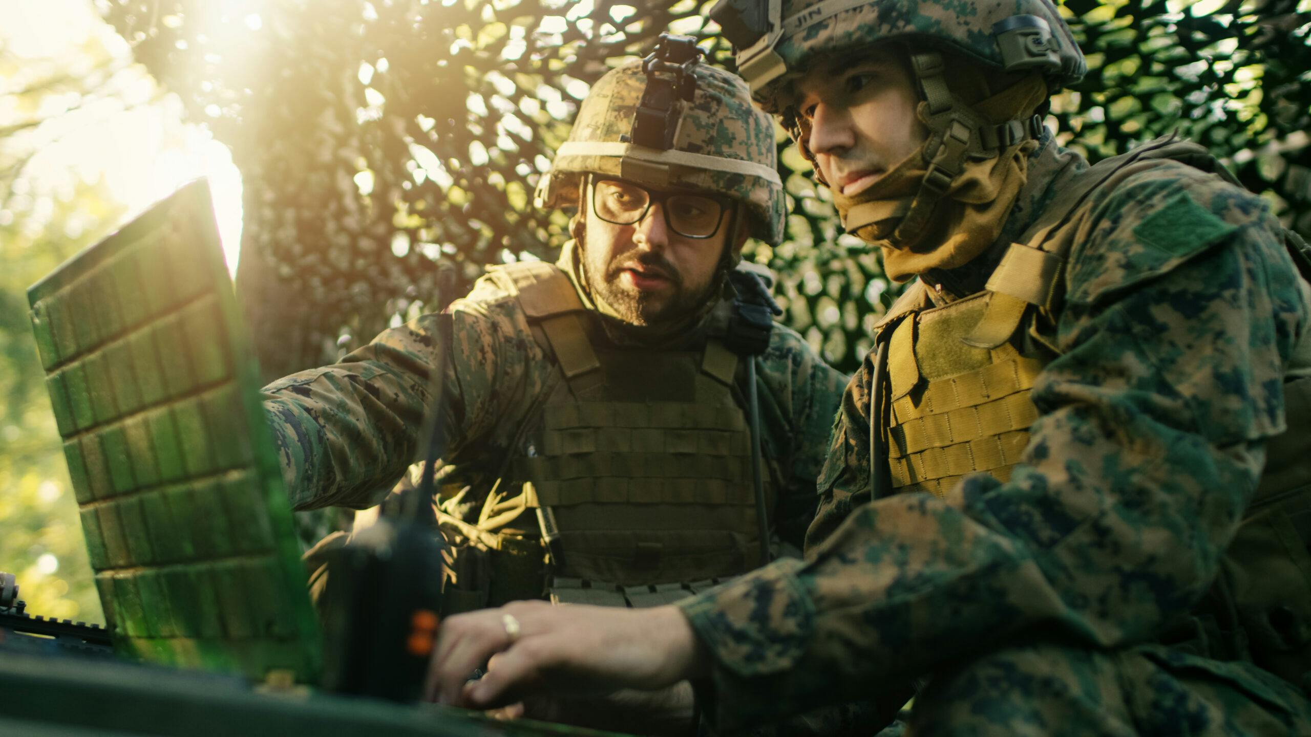 Image of two soldiers in full gear conferring over a field laptop.