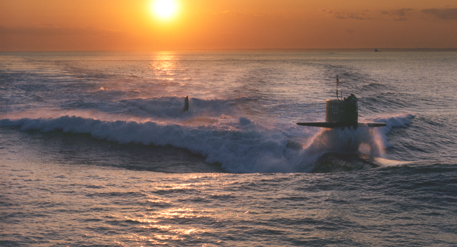 Naval submarine sailing across the sea at sunset