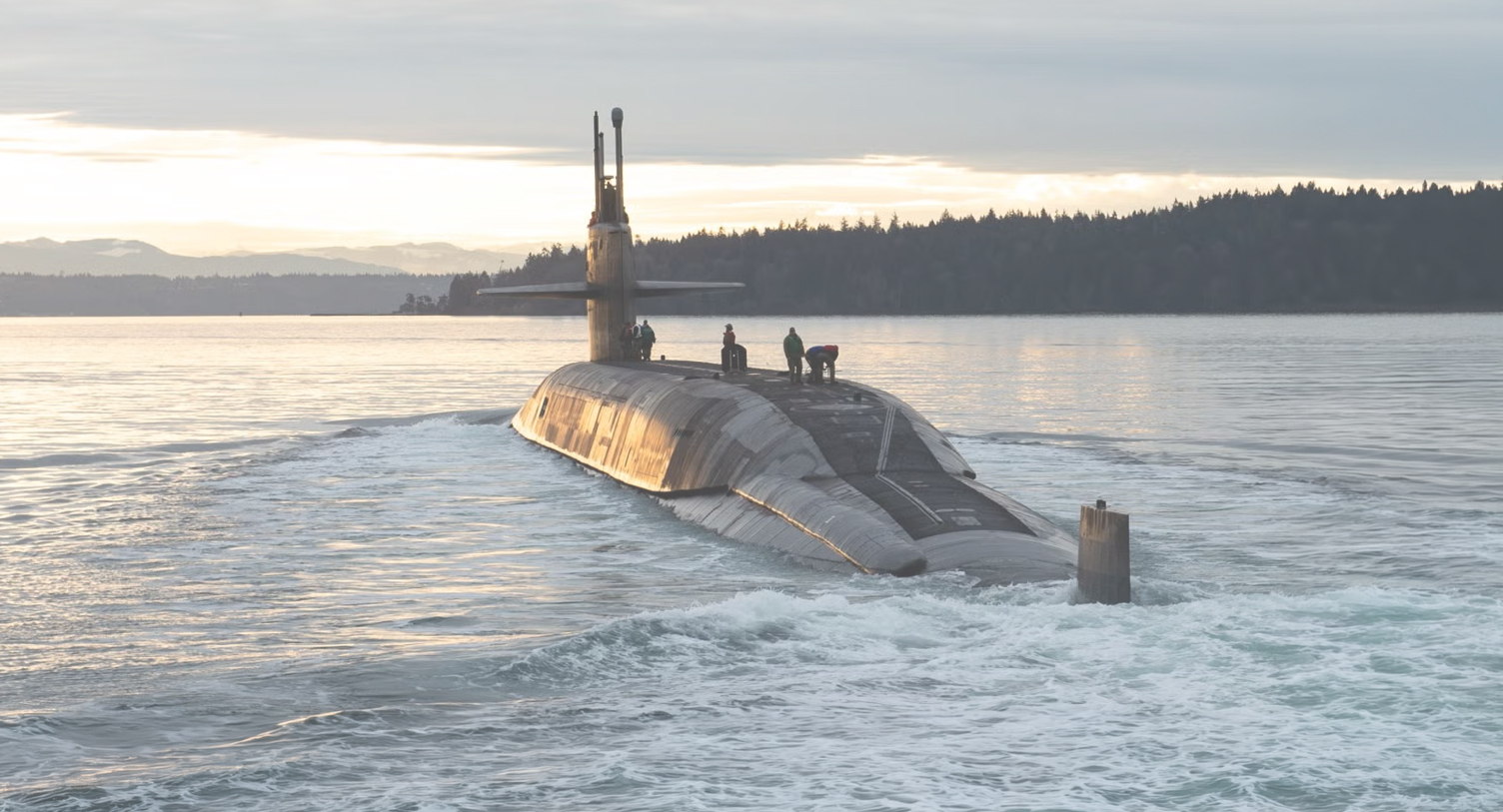 Naval submarine sailing across a tree lined body of water